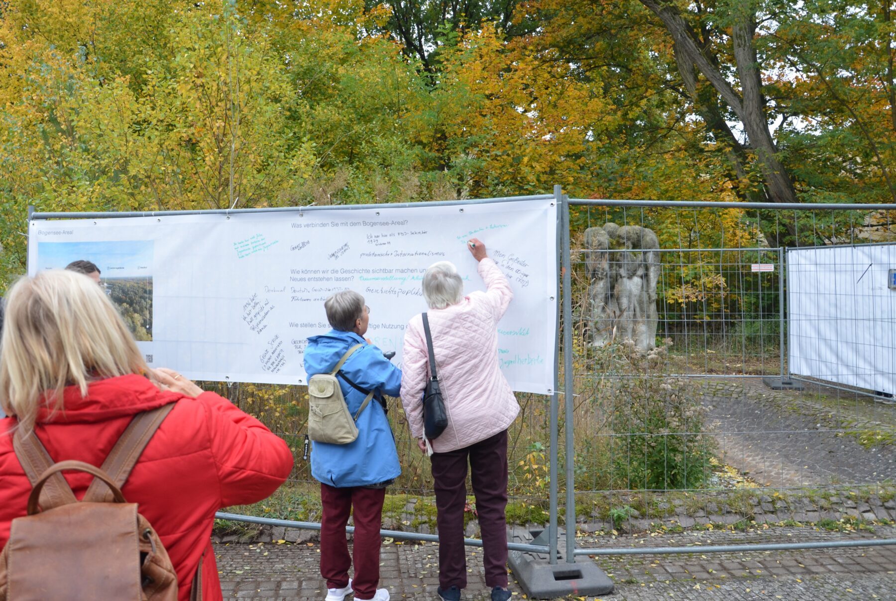 Zwei Menschen schreiben auf ein Plakat an einem Bauzaun.
